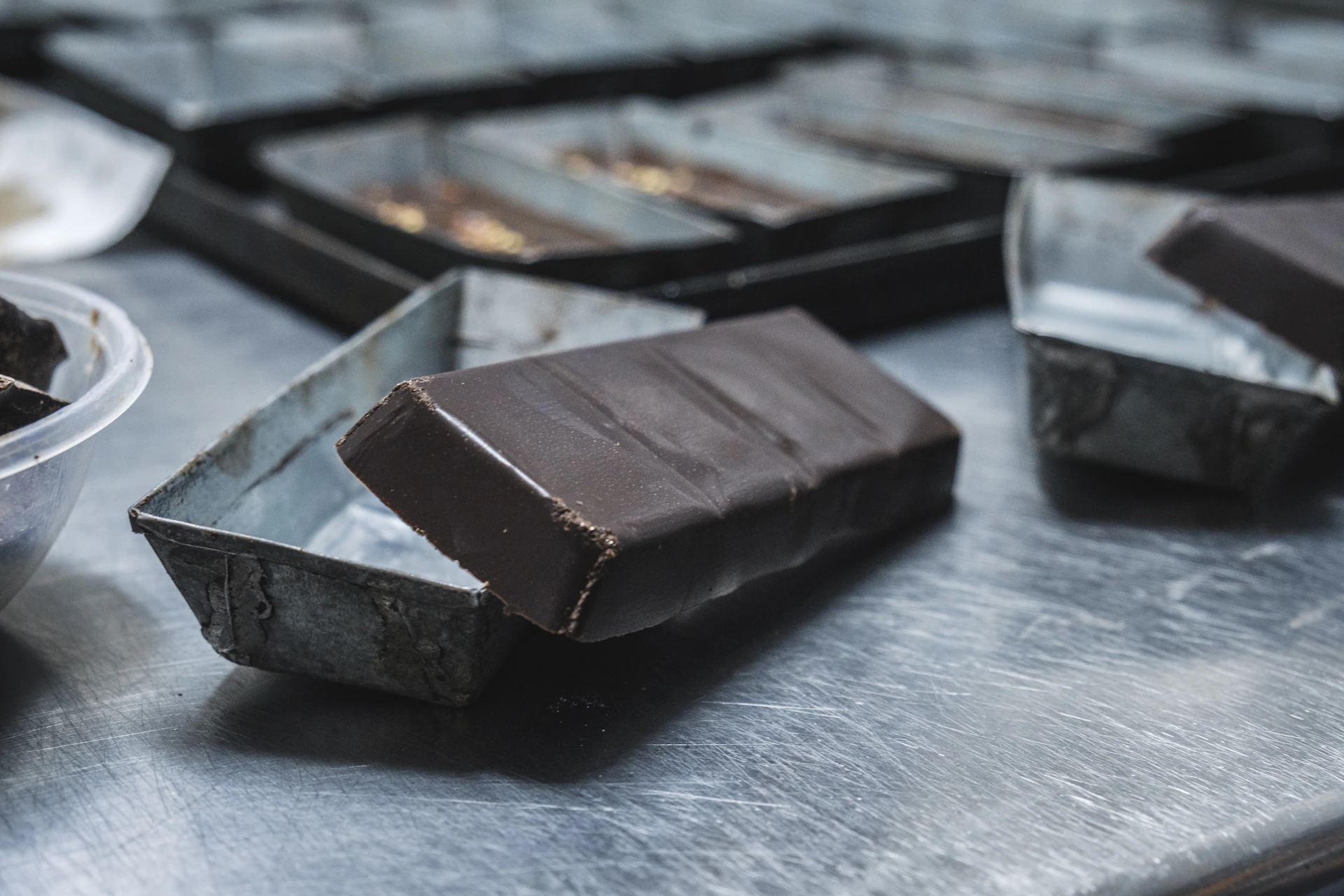 Close-up of a vibrant chocolate compound bar melting slightly on a rustic wooden table, surrounded by cocoa beans and baking tools.