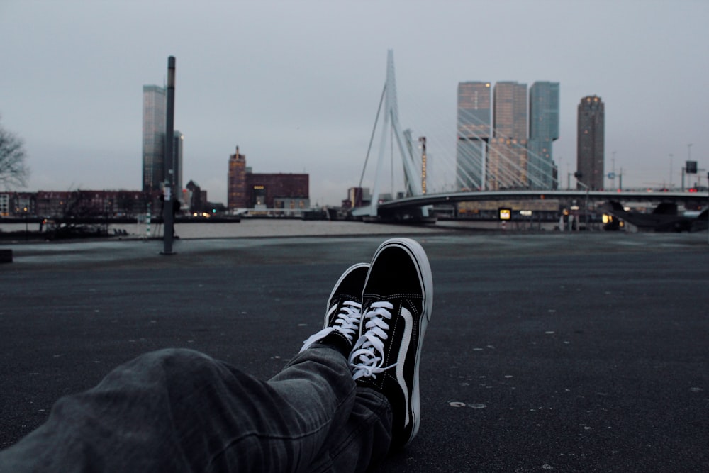 person sitting on grey concrete road in front of white suspension bridge