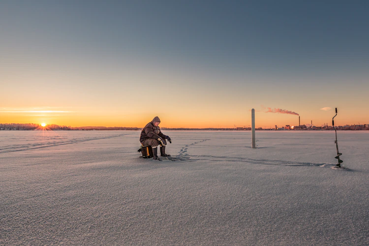 ice fisherman drilling a hole with a manual auger on a frozen lake