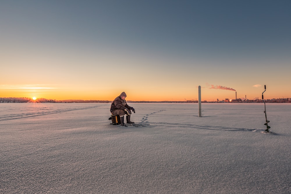 Persona sentada en taburete en un campo de hielo cerca de la barrena manual