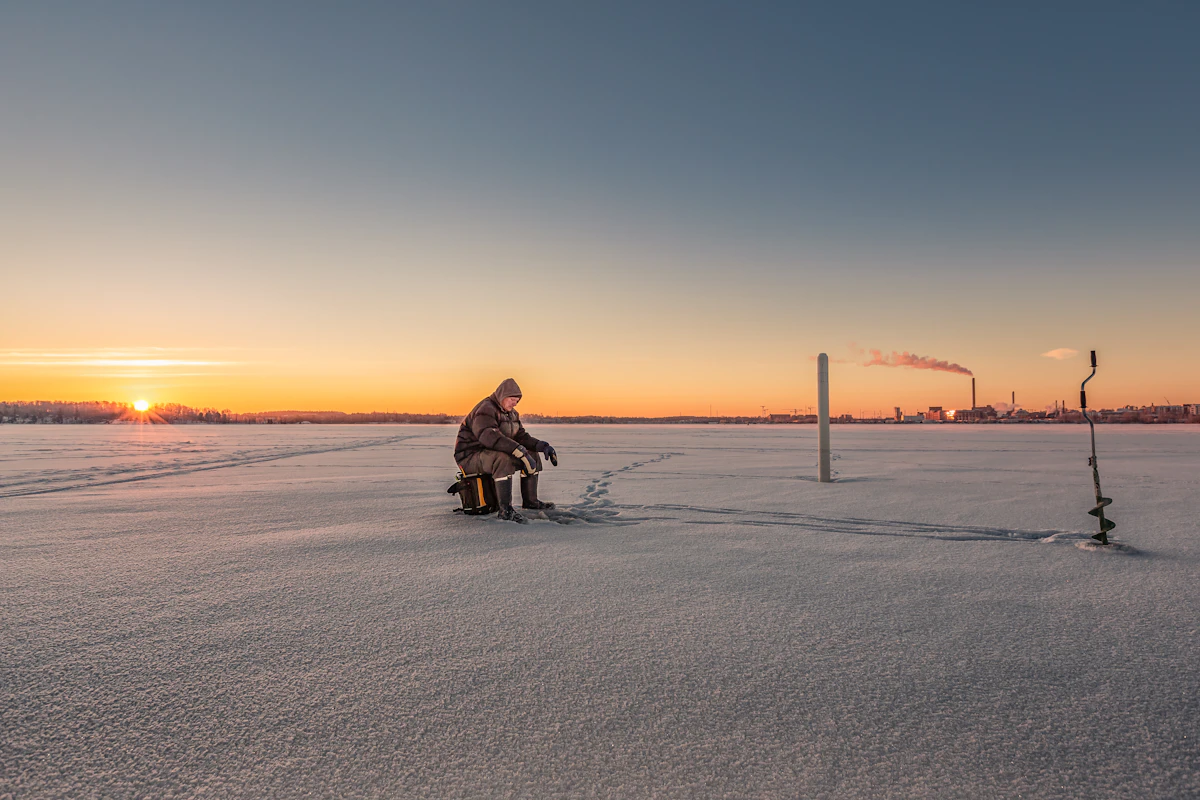 Angler seated beside an ice auger on a frozen lake