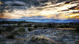 A rugged outback scene under a wide, glowing sunset sky.