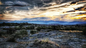 A rugged outback scene under a wide, glowing sunset sky.