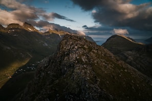 A dramatic mountain landscape with dynamic clouds and realistic light casting long shadows over rocky terrain.