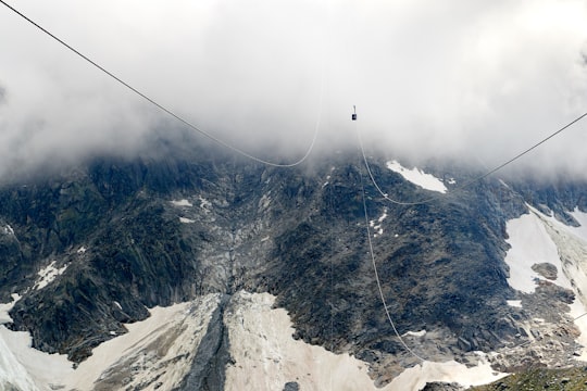 photo of cable car covered with white fog on top of green and white mountain in Aiguille du Midi France