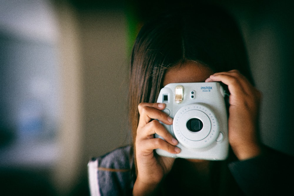 흰색 후지 필름 인스탁스 미니를 사용하여 사진을 찍는 여자