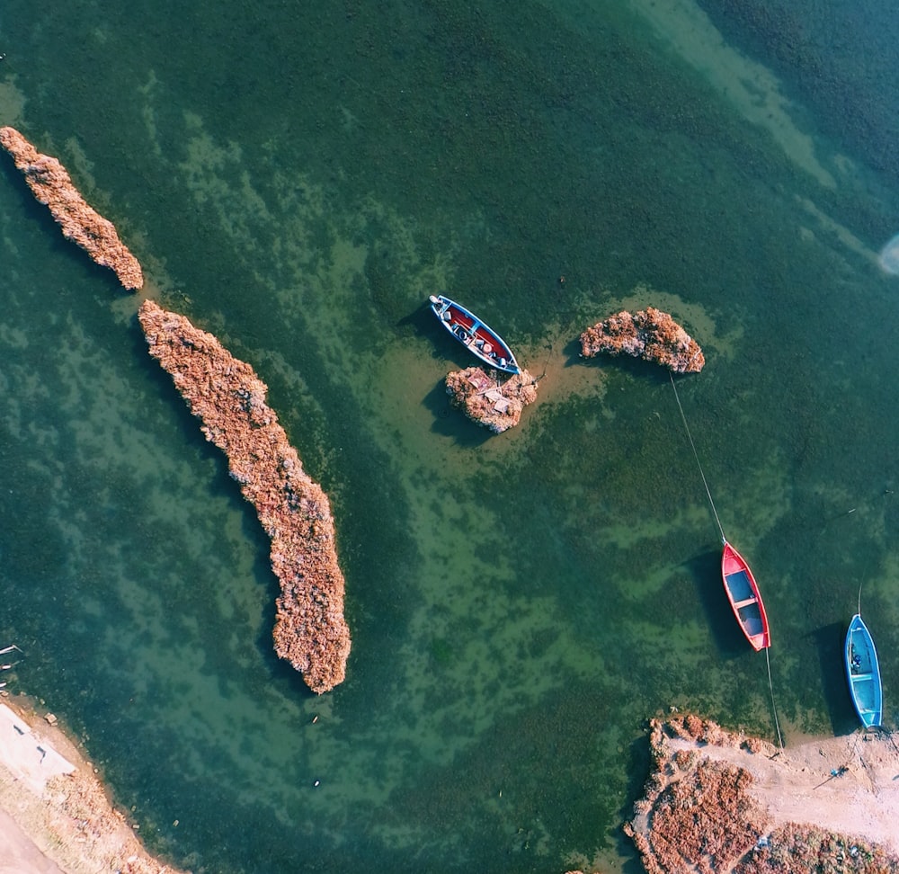 Fotografie aus der Vogelperspektive von drei verschiedenfarbigen Booten, die an weißen Felsen angedockt sind