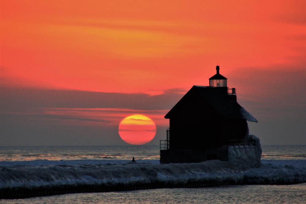 silhouette of house beside ocean during orange sunset