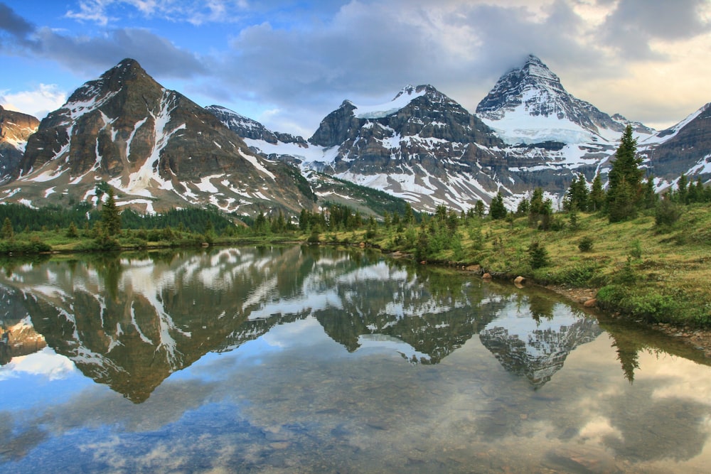 calm body of lake near grass and glacier mountain under white cloud blue skies