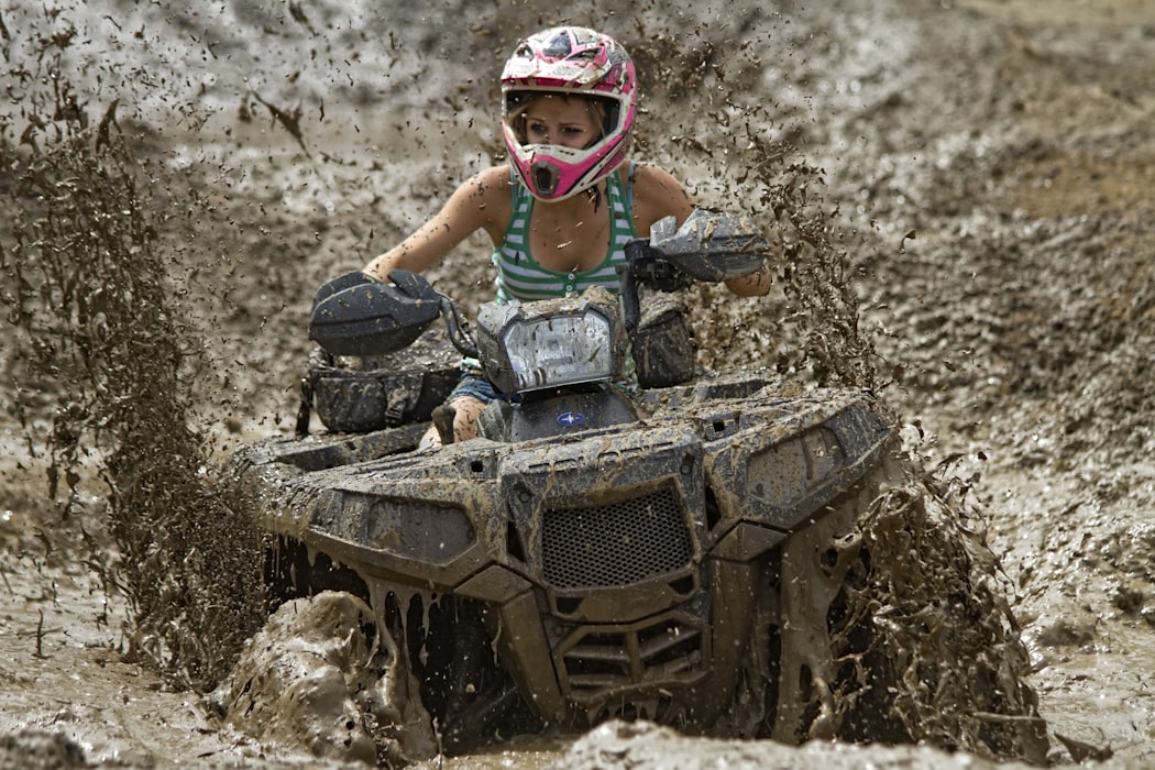 Woman riding a 4 wheeler through a large pool of mud