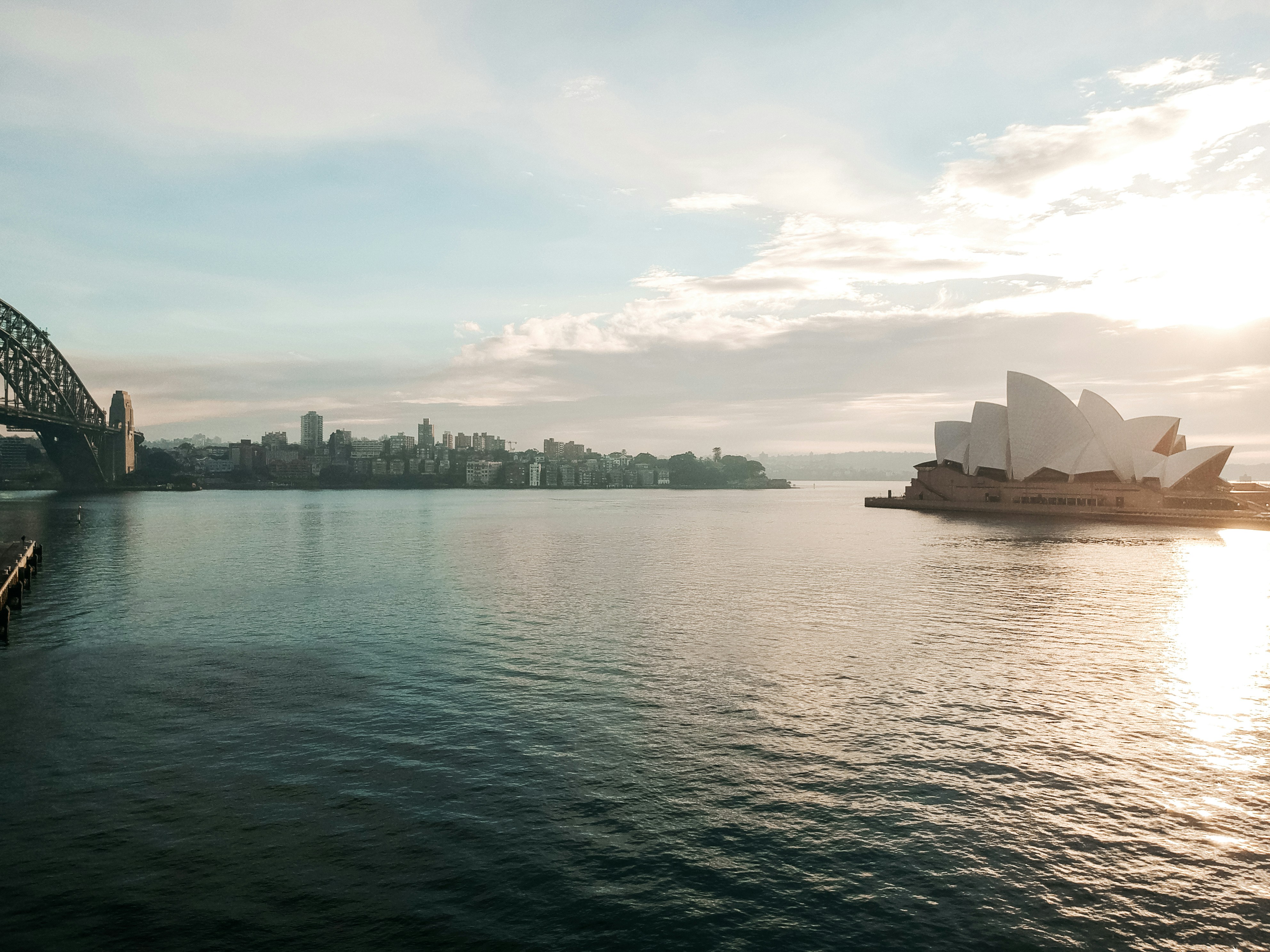 Sydney Opera House and Harbour Bridge at sunrise, warm golden light over calm blue harbour water