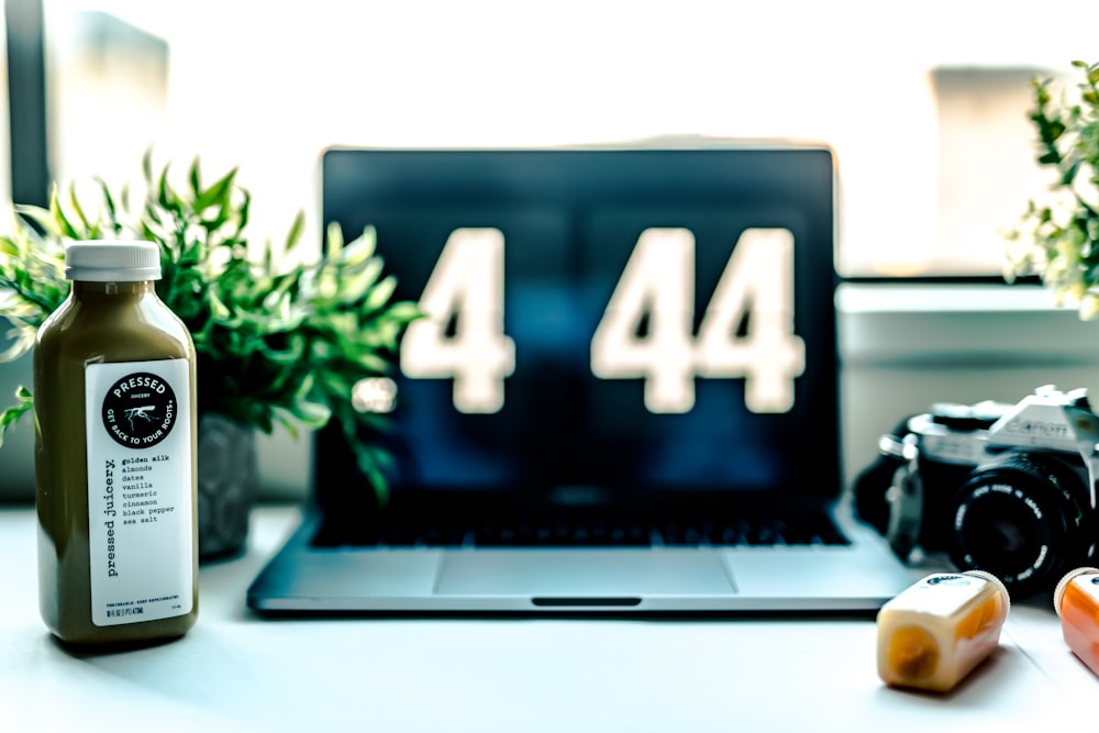 MacBook Pro displaying .4 44 beside camera and bottle