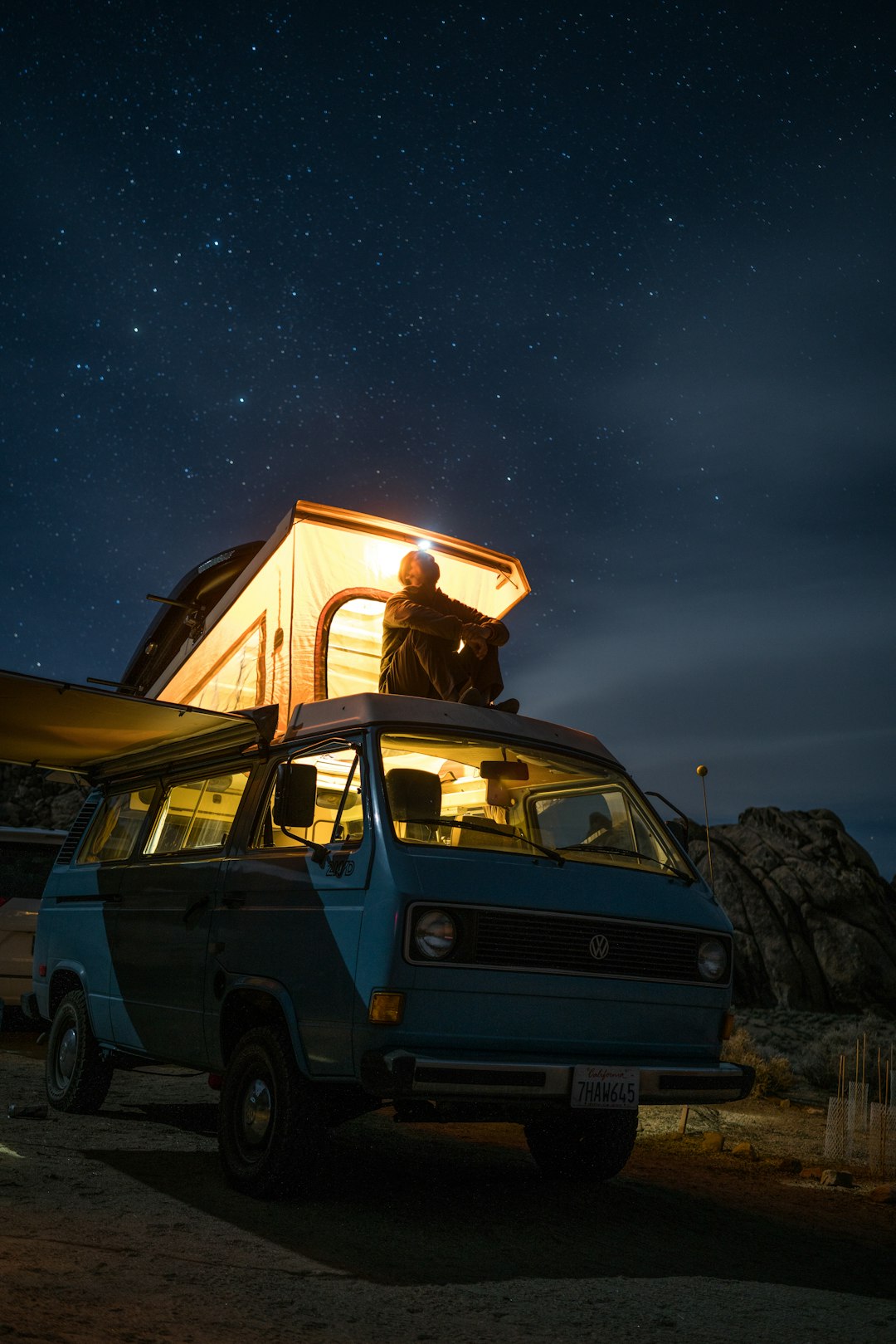 man sitting on top of blue van staring at sky during nighttime