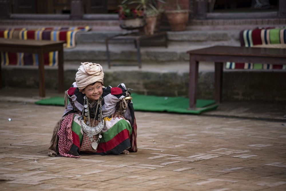 bambino che indossa vestito grigio e multicolore piegarsi bianco tenendo il ginocchio sul pavimento fotografia