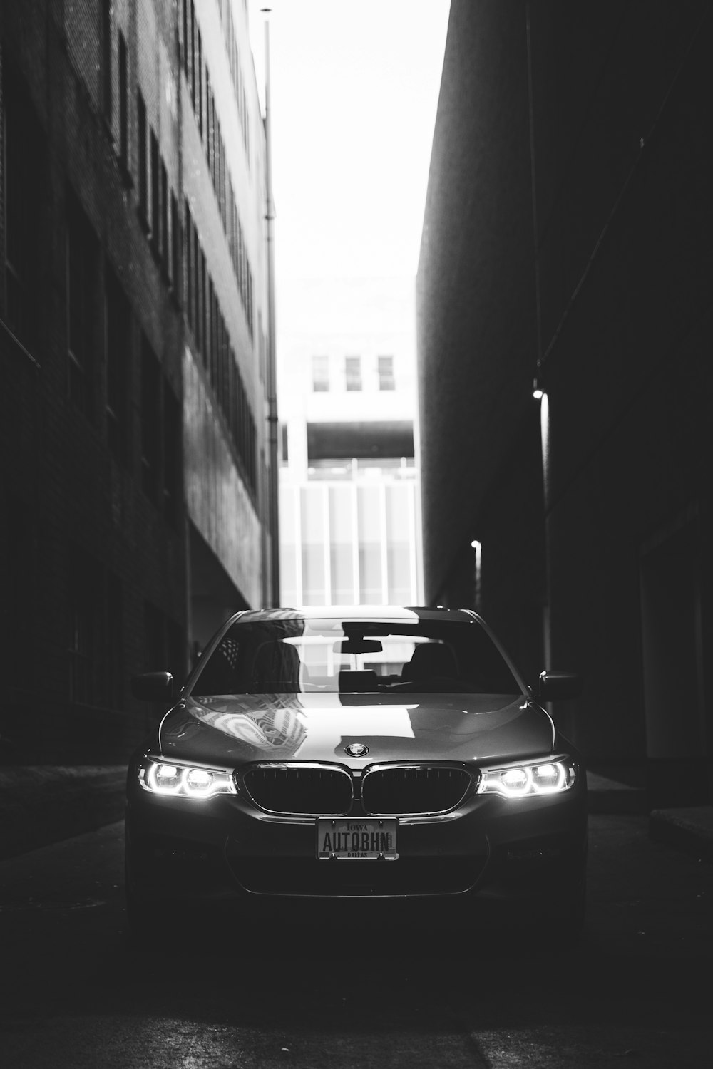 grayscale photo of BMW car parked between buildings