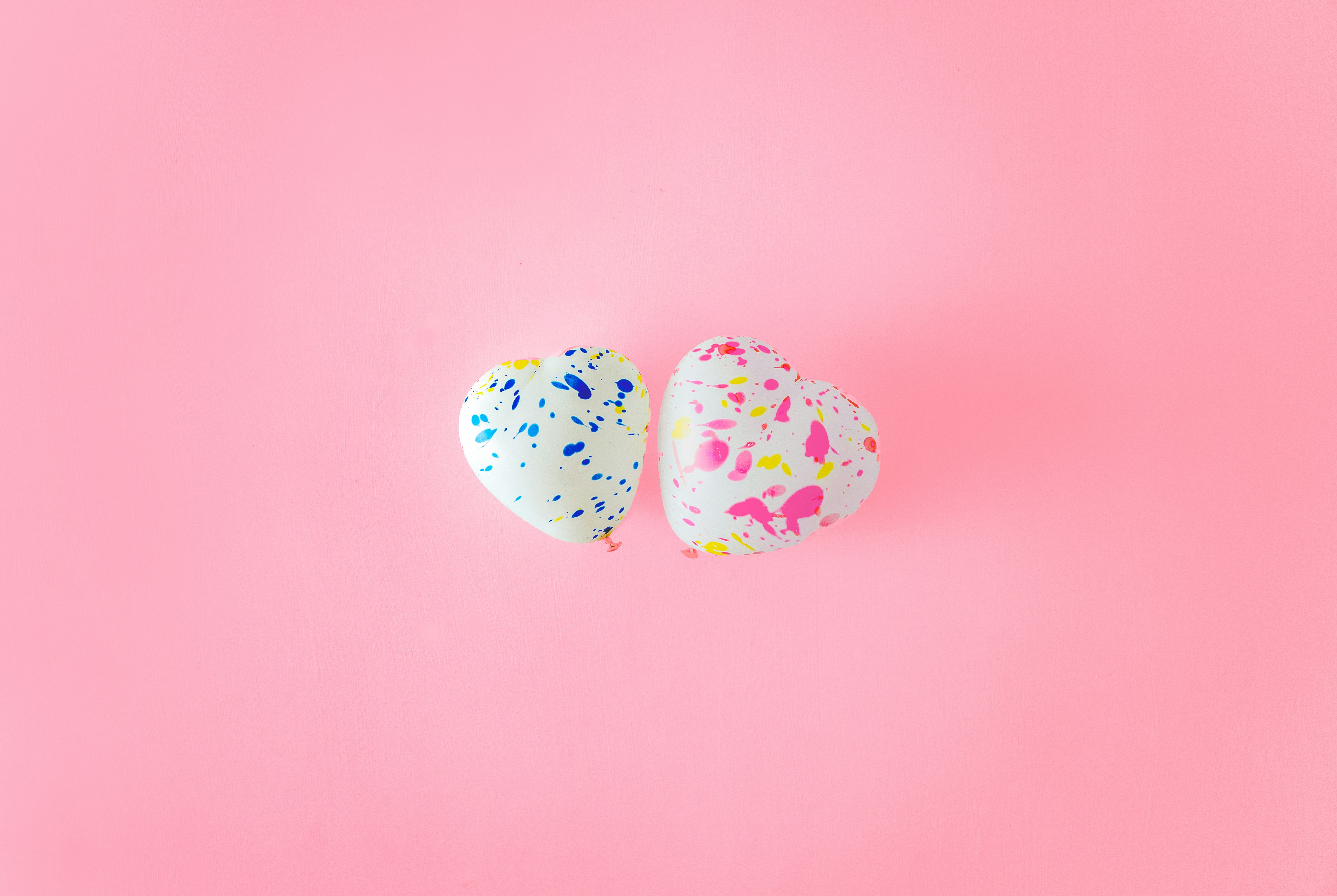 two heart-shaped balloons on a pink background