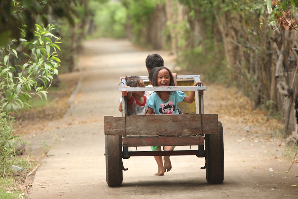 selective focus photo of two children riding on brown wooden cart