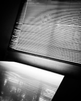 Abstract black and white photo of shadows cast by window blinds on a textured wall.