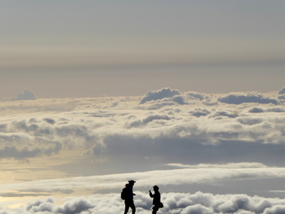 silhouette of two people overlooking clouds during daytime