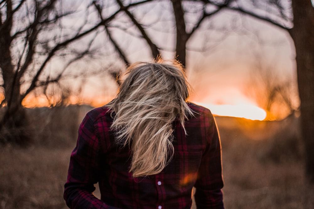 selective focus photography of blonde-haired man wearing red-and-black plaid dress shirt near trees during golden hour