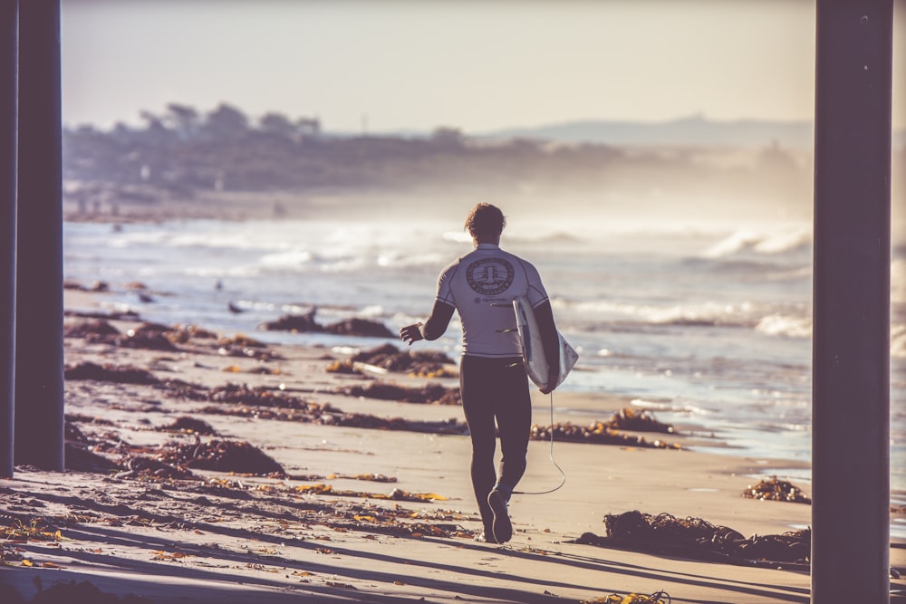 Hombre que lleva una tabla de surf blanca caminando hacia la playa