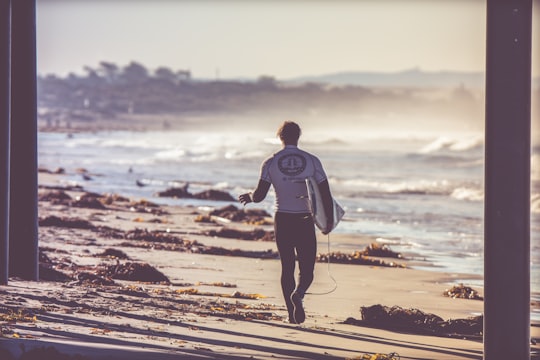 man carrying white surfboard walking towards beach in Pismo Beach United States