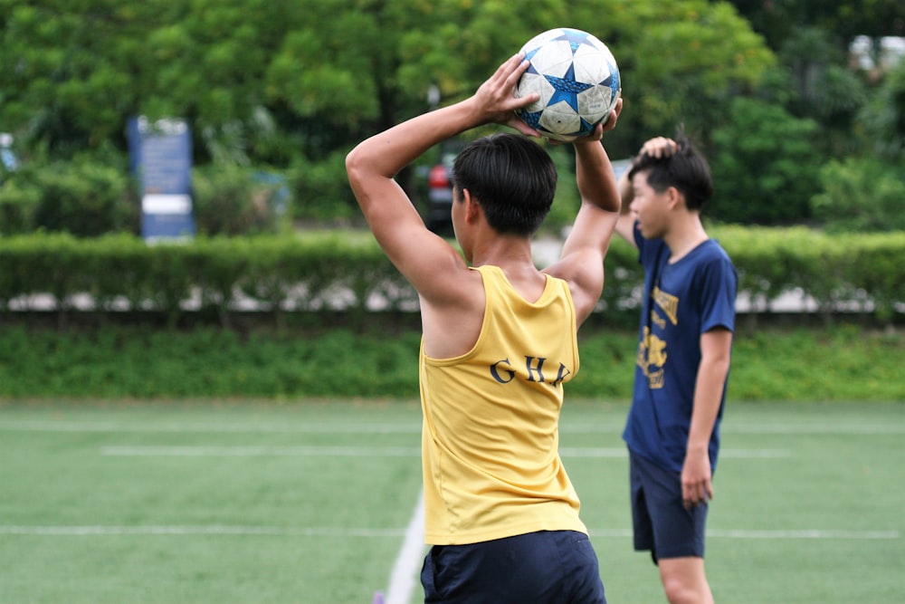 man wearing yellow tank top holding soccer ball