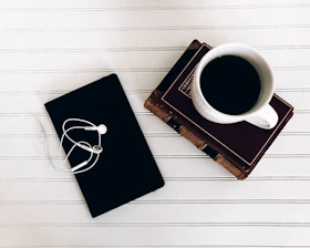 A minimalist desk setup with an open book, a notebook, and a coffee cup on a clean white surface.