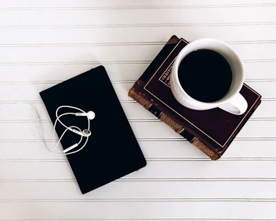 A minimalist desk setup with an open book, a notebook, and a coffee cup on a clean white surface.
