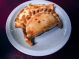 Golden-brown baked pastries are neatly arranged on a white ceramic plate with a dark background.
