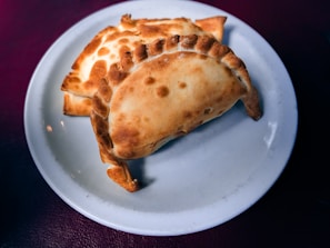 Golden-brown baked pastries are neatly arranged on a white ceramic plate with a dark background.