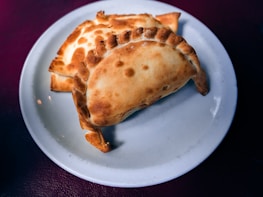 Golden-brown baked pastries are neatly arranged on a white ceramic plate with a dark background.