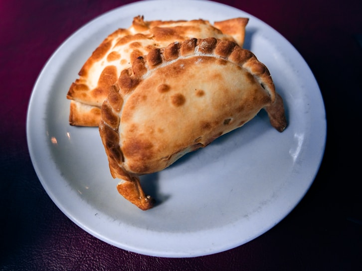 Golden-brown baked pastries are neatly arranged on a white ceramic plate with a dark background.