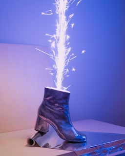Silver boots with angular designs standing on a cracked concrete floor lit by soft blue light.