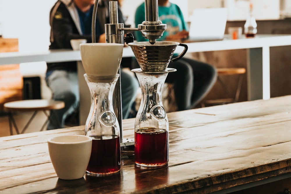 Deux bouteilles en verre transparent avec des liquides rouges sur un comptoir en bois rbown