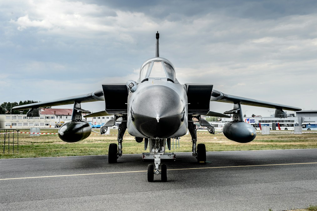 Avion de combat stationné face à l’objectif sur un tarmac, sous un ciel nuageux