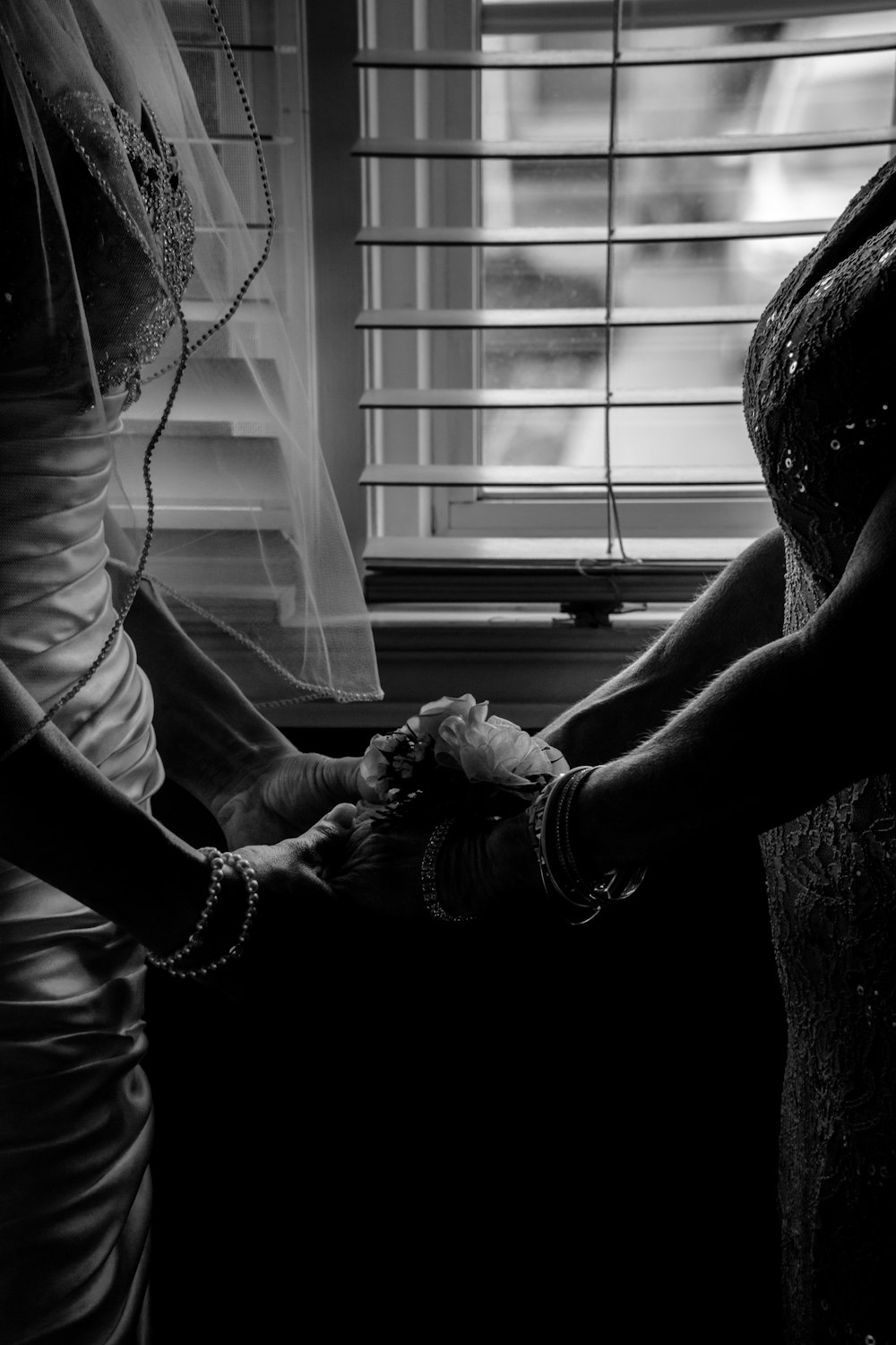 grayscale photography of two woman holding hands near window blinds