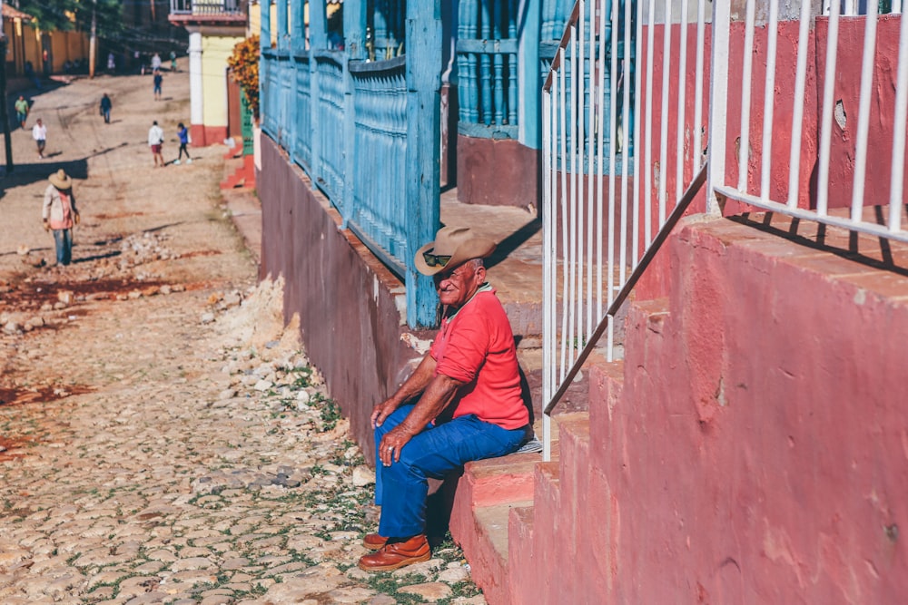 man sitting on red concrete stair in front of house during daytime