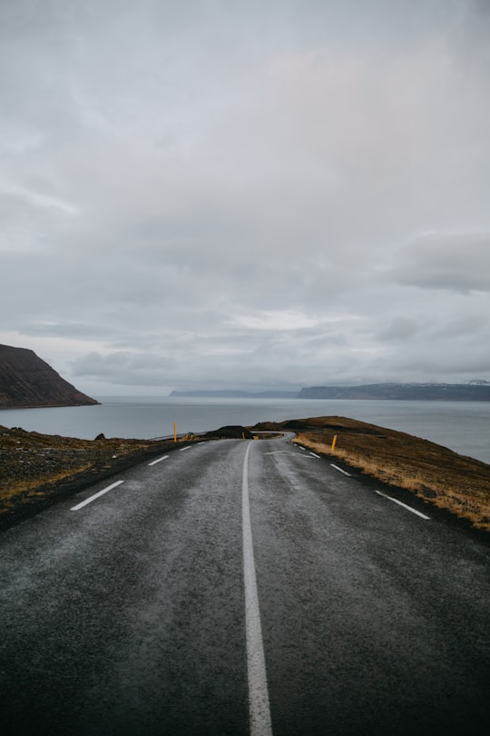 gray asphalt road going on the body of water in Súðavík Iceland