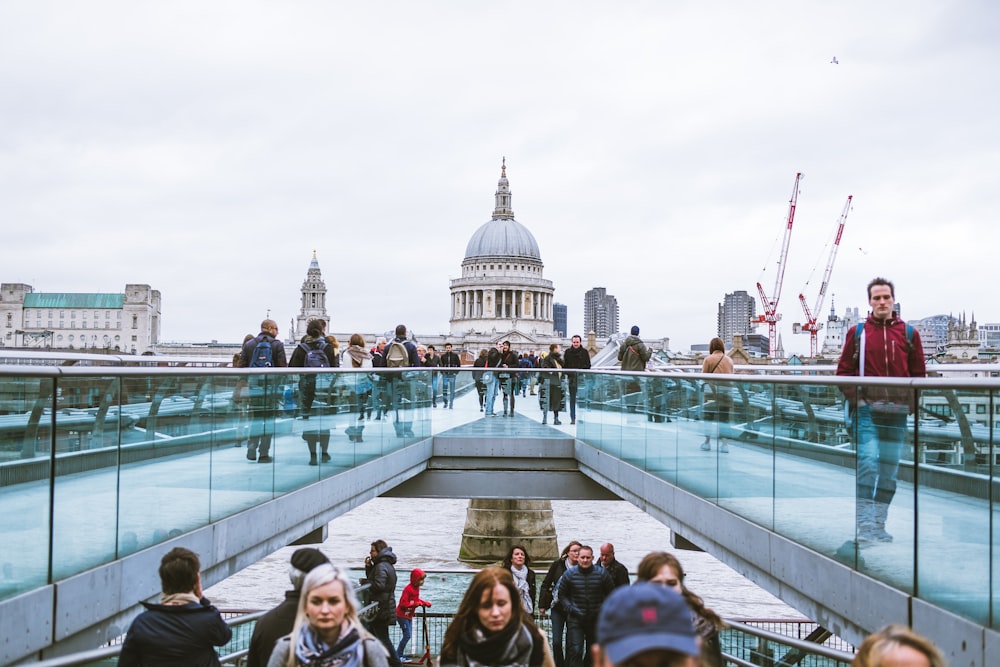 people on white bridge with blue glass rails near white domed building during daytime