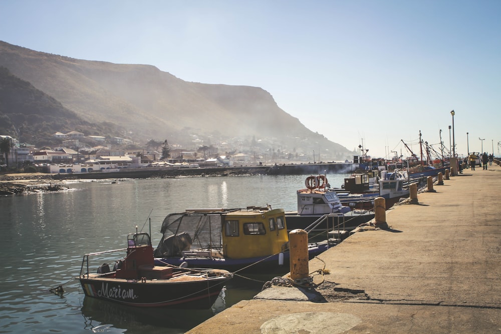 assorted-color motorboats dock on brown concrete pier near mountain during daytime