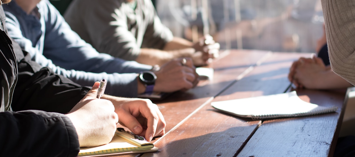 people sitting on chair in front of table while holding pens during daytime