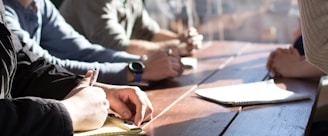 people sitting on chair in front of table while holding pens during daytime