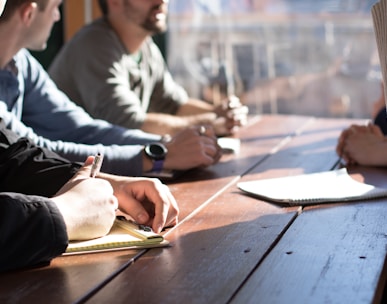 people sitting on chair in front of table while holding pens during daytime