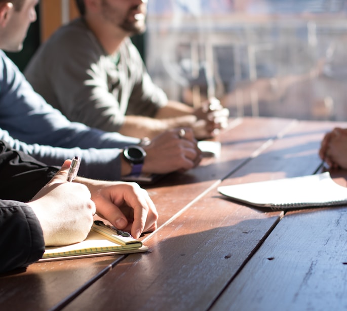 people sitting on chair in front of table while holding pens during daytime