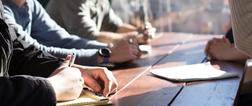 people sitting on chair in front of table while holding pens during daytime