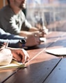 people sitting on chair in front of table while holding pens during daytime