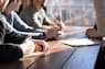 people sitting on chair in front of table while holding pens during daytime