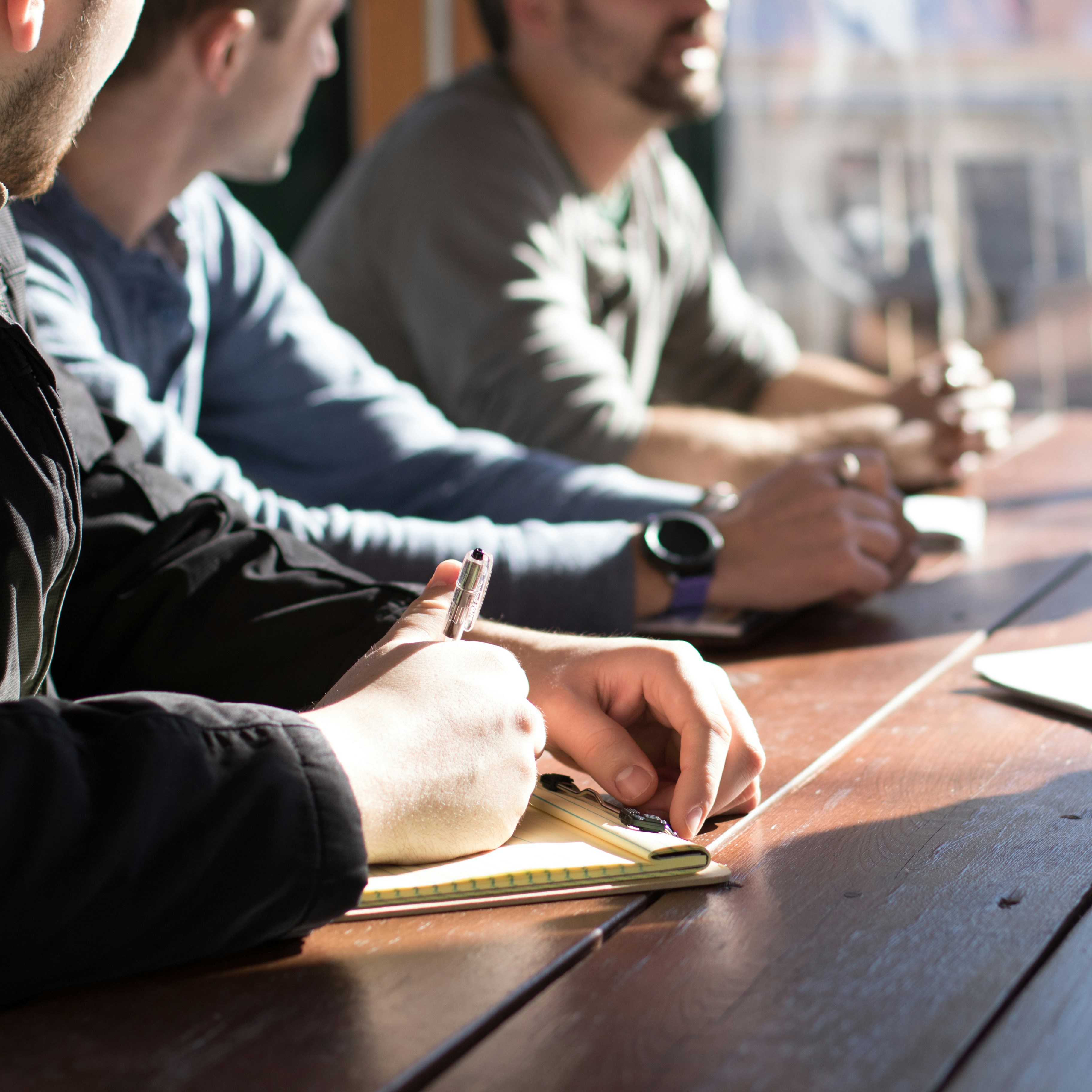 people sitting on chair in front of table while holding pens during daytime