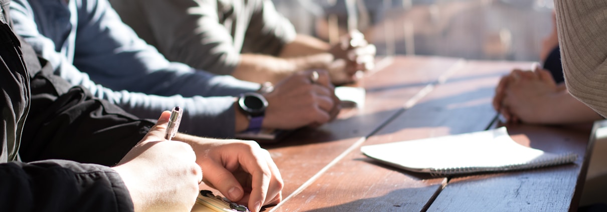 people sitting on chair in front of table while holding pens during daytime